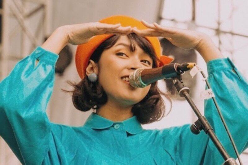 Vira Talisa menyanyi dengan mic, mengenakan kemeja biru dan topi berwarna orange